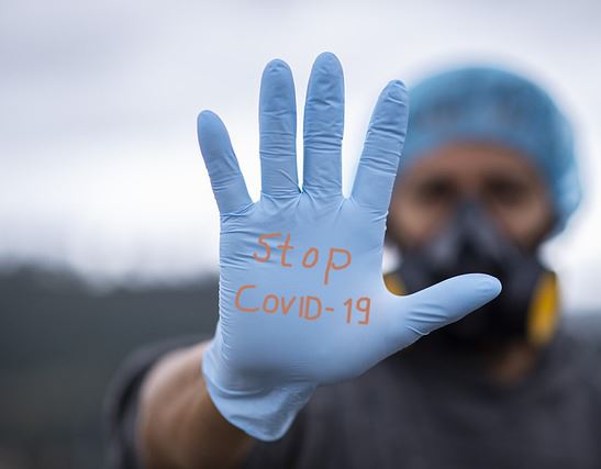 Man wearing a surgical glove with Stop Covid-19 written on his palm